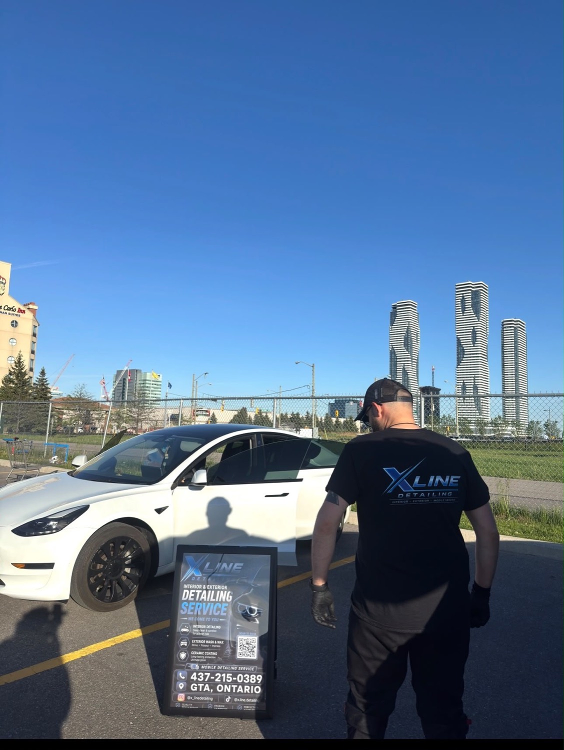 X Line Detailing technician detailing a white Tesla with the Mississauga skyline behind